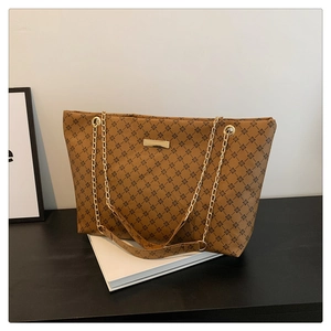 Close-up of brown tote bag featuring black floral patterns and gold chain strap detail