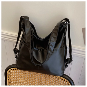 Gros plan du sac cabas noir en similicuir brillant suspendu à une chaise en rotin