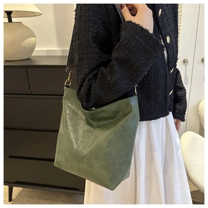 Détail du sac seau en cuir vert foncé avec large bandoulière brodée et boucle dorée