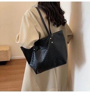 Detail of black woven leather tote bag featuring a Fashion plaque and long shoulder straps
