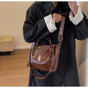 Dettaglio della borsa a secchiello in pelle cerata marrone con tracolla larga etnica