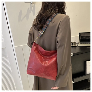 Détail du sac seau en cuir rouge avec bandoulière brodée ethnique et ferrures dorées