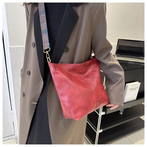 Gros plan d'un sac seau rouge vintage avec une large bandoulière décorative au motif ethnique