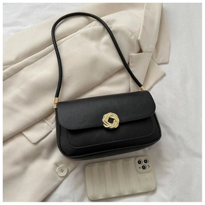 Détail d'un sac baguette noir en cuir avec boucle dorée tressée sur un blazer beige