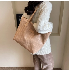 Detail of large woven leather tote bag with elegant texture worn on a woman's shoulder