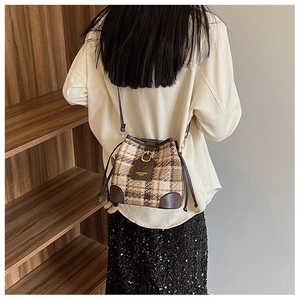 Detail of wool plaid bucket bag with drawstring closure and brown leather trim on model