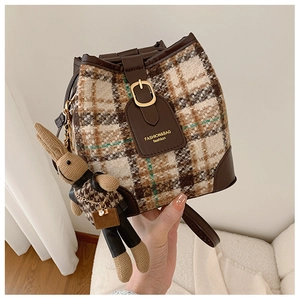Detail of plaid bucket bag featuring brown leather trim and a cute woven rabbit pendant