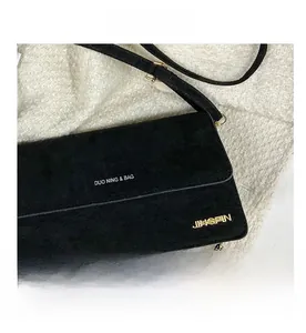 Nahaufnahme der mattschwarzen Wildleder-Umhängetasche mit weißem Schriftzug und Goldlogo