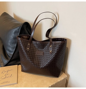 Detail of large brown woven tote bag with FASHION label on a stone surface