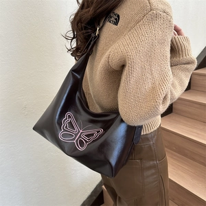 Brown leather tote bag with pink butterfly embroidery worn by model on stairs