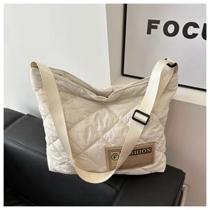 Détail du sac matelassé crème avec un écusson en cuir brun sur un canapé en cuir noir