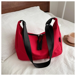 Sac bandoulière demi-lune rouge en nylon avec large sangle noire dans un décor de chambre