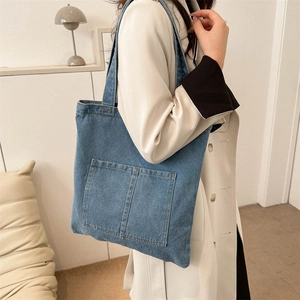 Grand sac cabas en jean bleu avec poches avant porté sur un trench-coat classique
