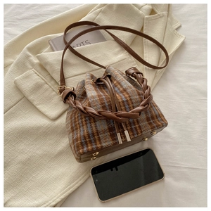 Detail of wool plaid bucket bag with woven handle and leather trim on soft background
