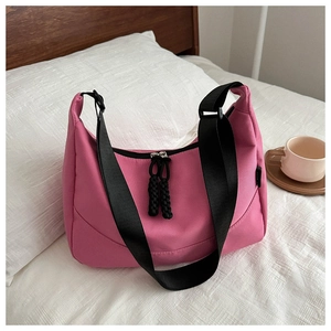 Sac hobo rose imperméable avec bandoulière réglable posé sur un lit blanc douillet