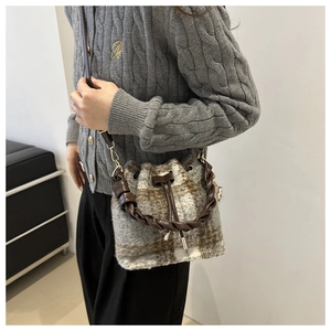 Detail of drawstring plaid bucket bag with brown woven leather handle and crossbody strap