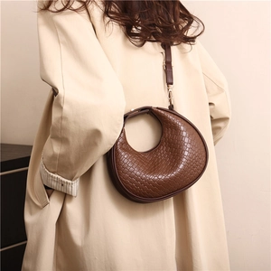 Borsa a mezzaluna intrecciata marrone scuro alla moda con tracolla regolabile su un trench