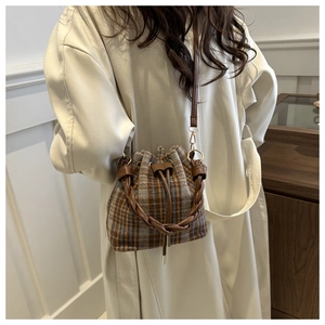Winter plaid bucket bag with woven handle shown on model wearing a beige wool coat