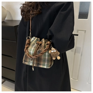 Detail of wool plaid bucket bag with drawstring closure and plush pendant on black coat