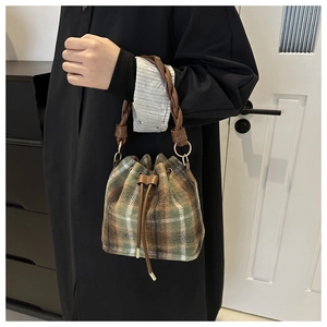 Detail of wool plaid bucket bag showing woven handle and green-brown checkered texture