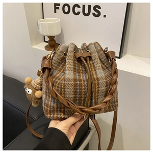 Detail of tweed bucket bag featuring woven handle and plush bear charm decoration