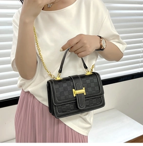 Détail d'un sac bandoulière noir avec texture en damier et chaîne dorée