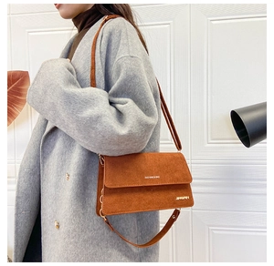 Nahaufnahme der braunen Wildledertasche mit Goldlogo und Buchstabendruck auf Mantel