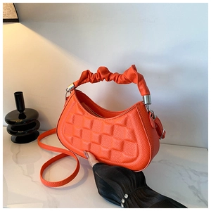Detail view of bright orange leather handbag with pleated handle and embossed pattern