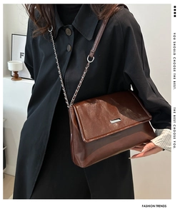 Detail of a vintage dark brown glossy leather chain shoulder bag on a model