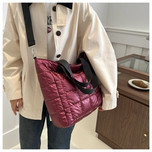 Close-up of wine red quilted tote bag with wide black strap and polished metal hardware