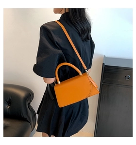 Close-up of bright yellow handbag with curved flap held by model in black dress