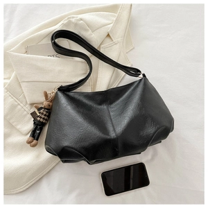 Detail of black pleated hobo bag texture with a cute teddy bear charm accessory