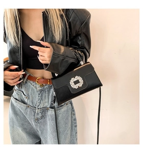 Detail view of a black crossbody bag with a square rhinestone buckle on a stylish model