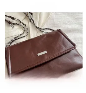 Detailed macro view of dark brown chain shoulder bag with glossy oil wax leather texture