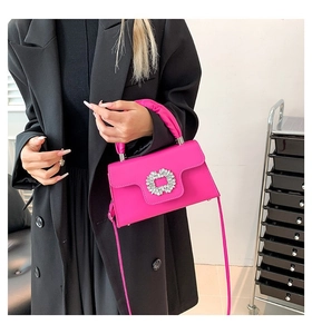 Detail of rose red crossbody bag featuring a large square crystal buckle and pleated handle