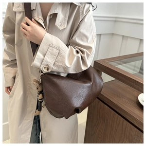 Detail of a dark brown pleated dumpling bag with a cute bear charm on a trench coat