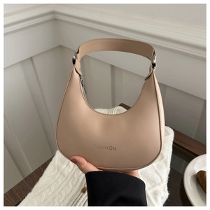 Close-up of beige hobo bag with silver Fashion logo held against a cozy home interior