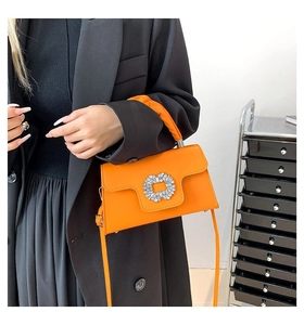 Detail of bright orange crossbody bag with a crystal buckle and pleated handle