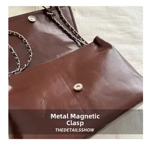 Detail shot of the magnetic metal buckle on a dark brown textured leather handbag