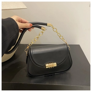 Détail du sac à rabat en cuir noir avec fermoir cylindrique doré et bandoulière chaîne