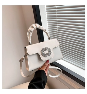 Detailed view of a white leather crossbody bag featuring a large crystal buckle and ruched handle