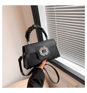 Detail of black leather crossbody bag featuring a rhinestone buckle and scrunchie handle