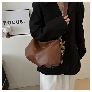 Brown oil-wax leather shoulder bag with plush bunny charm shown on a female model