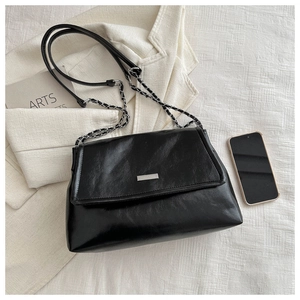Detail of black glossy leather flap handbag with silver chain strap and metal plate
