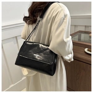 Detail of black faux leather tote bag with silver chain strap and subtle logo texture