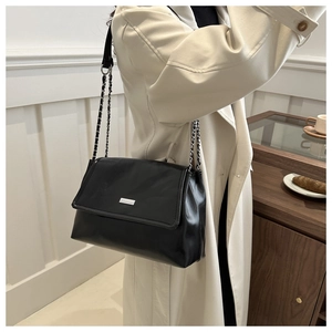 Detail of a black chain shoulder bag on a model wearing a beige trench coat