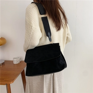 Matte suede tote bag with wide strap and gold hardware shown on model in minimal room