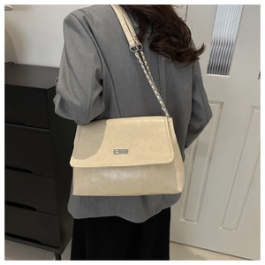 Detail of a beige leather flap bag with silver metal chain strap shown on a model