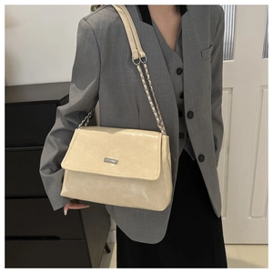 Close-up of cream white PU leather chain bag worn on shoulder over grey suit jacket