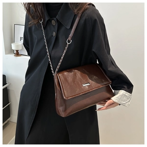 Detail of dark brown leather shoulder bag with silver chain strap and metal logo plaque